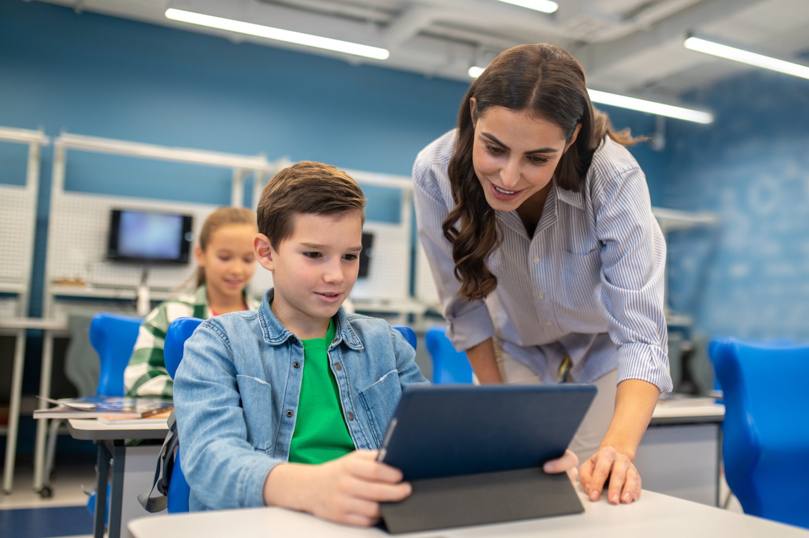 woman looking into tablet of student boy